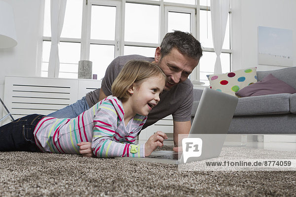 Vater und Tochter mit Laptop auf Teppich im Wohnzimmer