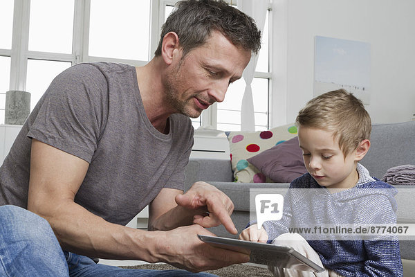 Father and son using tablet computer in living room