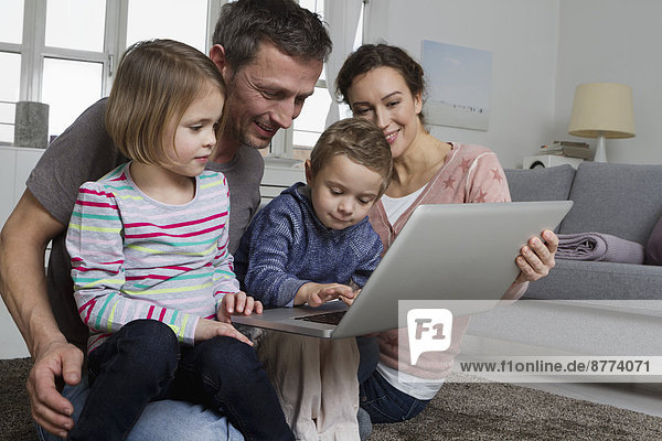 Glückliche vierköpfige Familie mit Laptop im Wohnzimmer