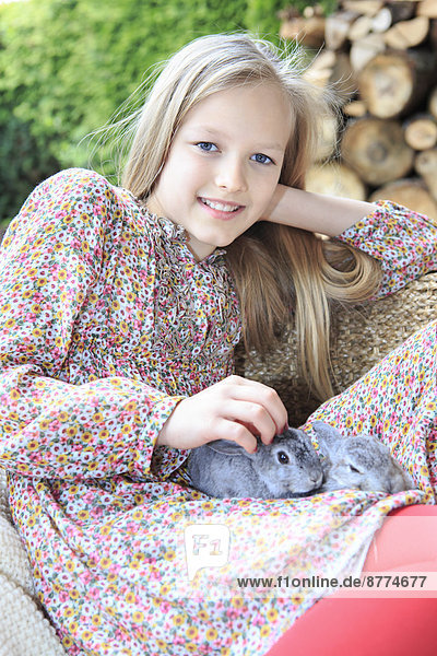 Porträt eines lächelnden Mädchens mit zwei Kaninchen auf dem Schoß