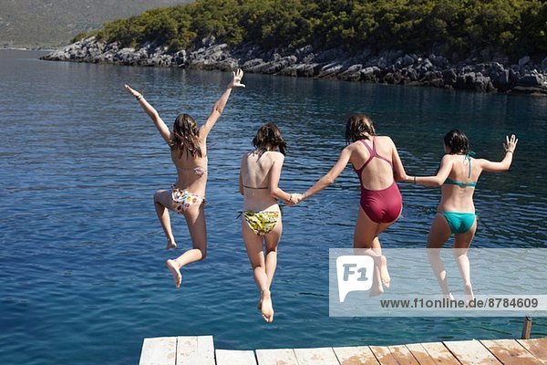 Vier Mädchen springen vom Pier ins Meer.