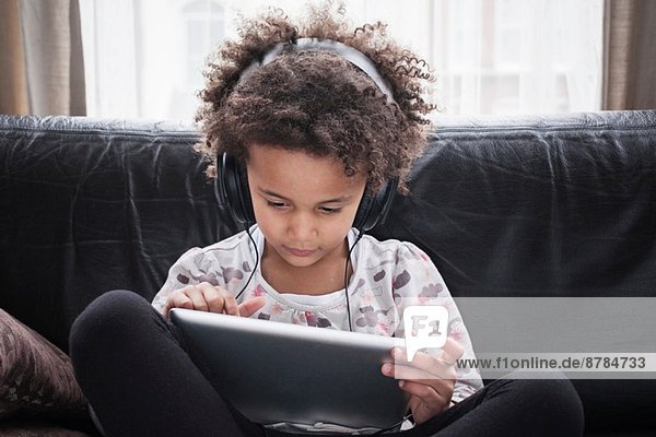 Mädchen auf dem Sofa sitzend mit digitalem Tablett und Kopfhörer