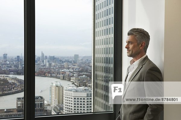 Portrait eines reifen Geschäftsmannes  der aus dem Bürofenster schaut  Canary Wharf  London  UK