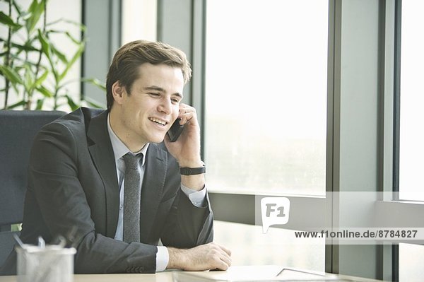 Junger Geschäftsmann im Gespräch mit dem Smartphone aus dem Büro