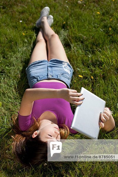 Teenagermädchen entspannt im Park beim Betrachten des digitalen Tabletts