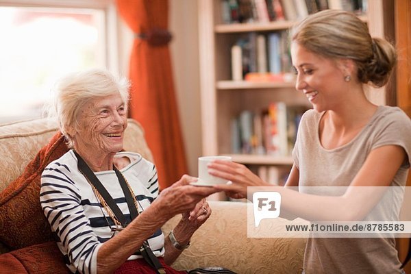 Care assistant handing coffee cup to senior woman