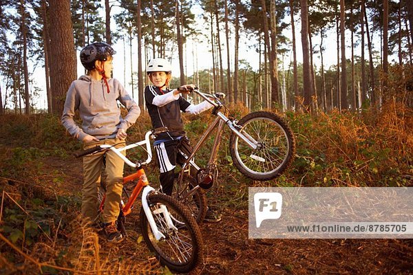 Twin brothers holding BMX bikes chatting in forest