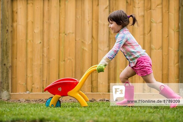 Junges Mädchen beim Laufen mit Spielzeugkarre im Garten