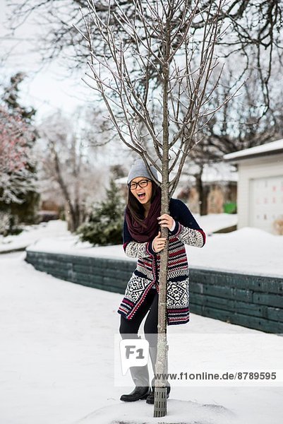 Junge Frau hält sich im Schnee an einem Baum fest