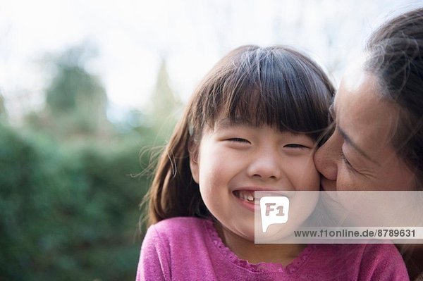 Mädchen wird von ihrer Mutter im Garten auf die Wange geküsst.