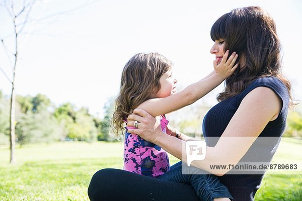 Mittlere erwachsene Frau mit junger Tochter im Park sitzend