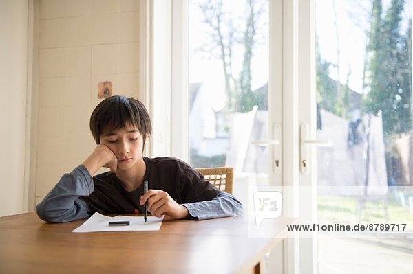 Boy sitting at table  holding pen to paper