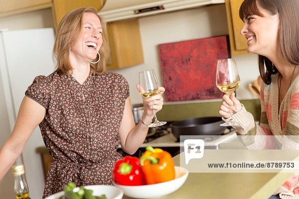Mid adult female friends drinking wine and laughing in kitchen