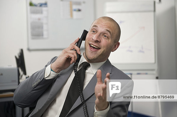 Young man wearing a suit is talking on a phone in the office