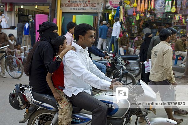 Young Indian Muslim family ride motorcycle in street scene in city of Varanasi  Benares  Northern India