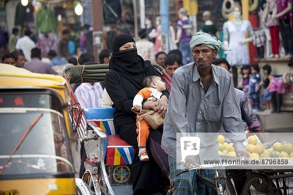 Muslim woman and child travel by rickshaw in crowded street scene in city of Varanasi  Benares  Northern India
