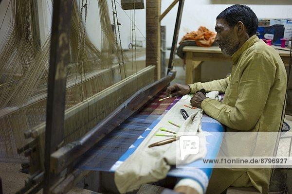 Indian man working loom at silk factory making textiles and saris at Bressler near Varanasi  Benares  Northern India