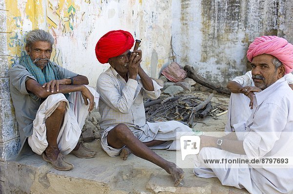 Indian man in traditional clothing smokes clay pipe while sitting with friends in Narlai village in Rajasthan  Northern India