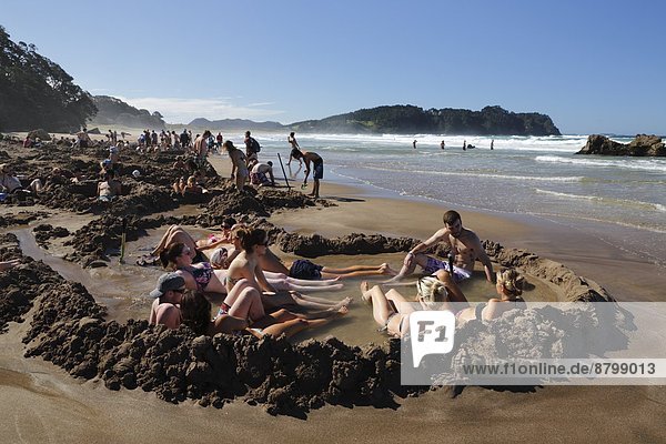 Tourists relaxing in hot pools dug on beach  Hot Water Beach  Coromandel Peninsula  Waikato  North Island  New Zealand  Pacific