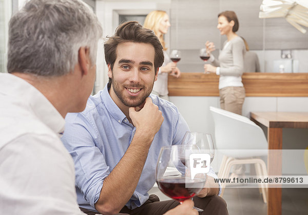 Zwei Männer mit Weinglas  im Hintergrund zwei Frauen mit Weinglas