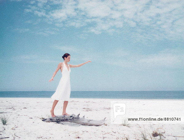 Frau balanciert auf Treibholz am Strand  Arme ausstrecken