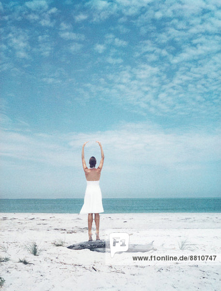 Frau auf Treibholz am Strand stehend  Arme erhoben  Rückansicht