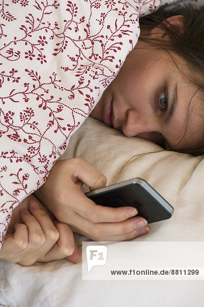Frau liegt Bett Blick auf Smartphone mit unglücklichem Ausdruck im Gesicht