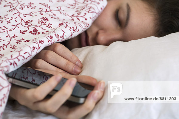 Frau schläft im Bett mit Smartphone in der Hand