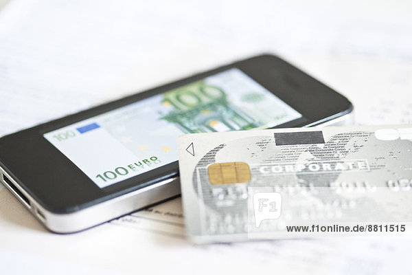Credit card resting on smartphone displaying one-hundred euro banknote