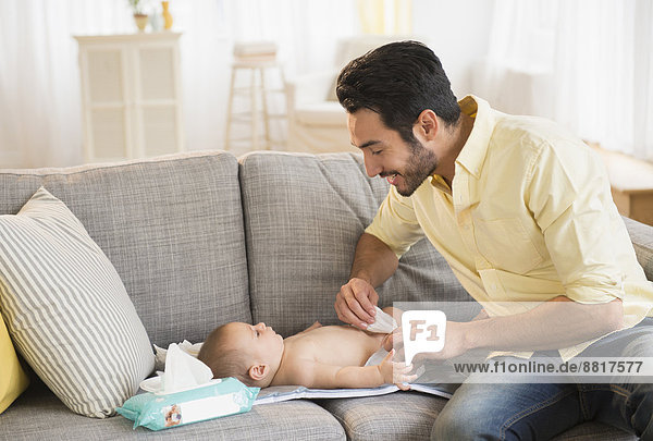 Father changing baby's diaper on sofa