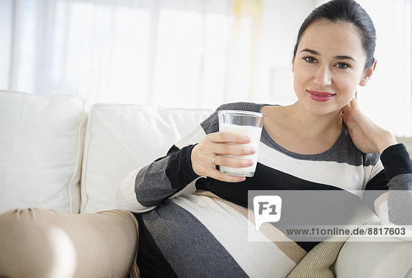 Pregnant Caucasian woman drinking milk on sofa
