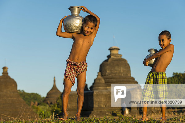Lächelnde Jungen beim Wassertragen vor Pagode oder Tempel  Mrauk U  Sittwe-Division  Rakhaing Staat  Myanmar
