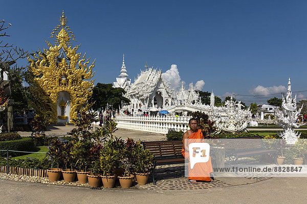 Mönch sitzt vor dem goldverzierten Eingang des Wat Rong Khun  Weißer Tempel  Architekt Chalermchai Kositpipat  Chiang Rai  Provinz Chiang Rai  Nordthailand  Thailand