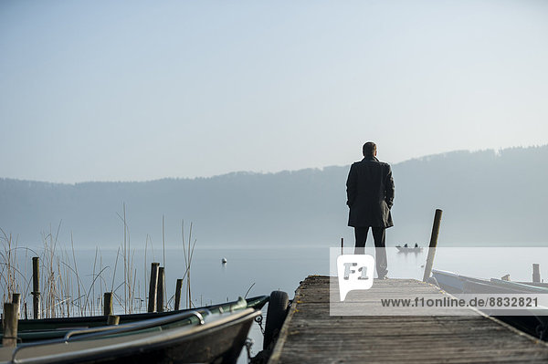 Mann steht auf Holzsteg und schaut auf den See.