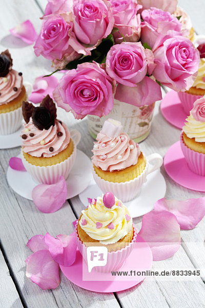 Cupcakes and flower vase of pink roses on wooden table