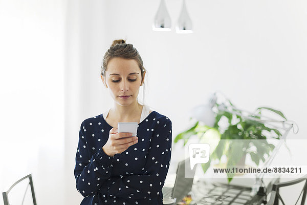 Junge Frau liest SMS auf dem Smartphone zu Hause