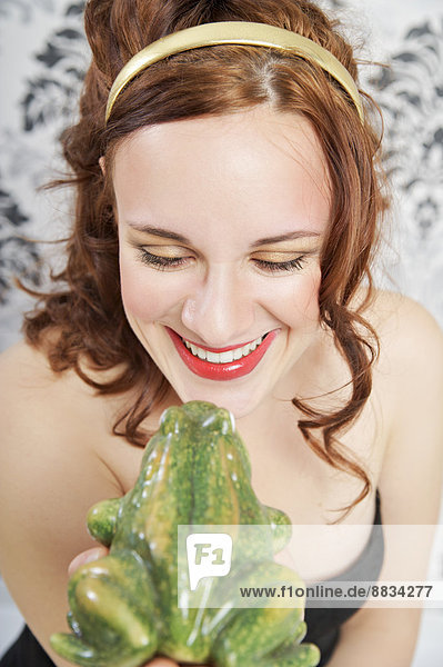 Porträt einer lächelnden jungen Frau  die einen Frosch küsst.