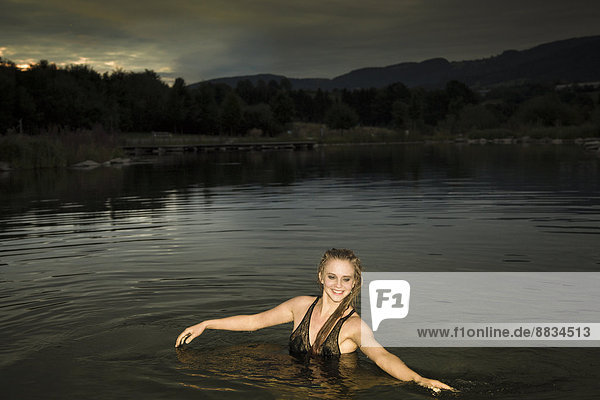 Young woman bathing with evening dress in lake at dawn