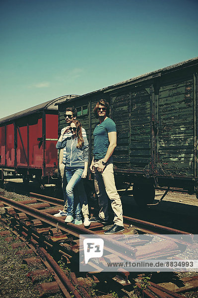 Drei Freunde mit Sonnenbrille stehen vor dem alten Güterwagen