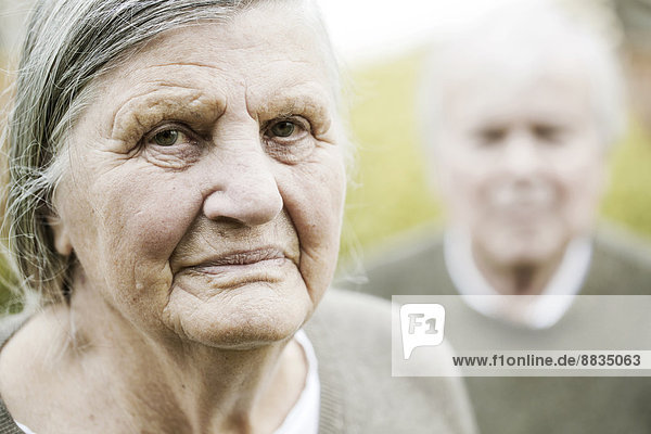 Porträt einer älteren Frau mit Mann im Hintergrund