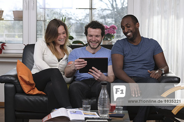 Drei Freunde haben Spaß mit dem Tablet-Computer zu Hause