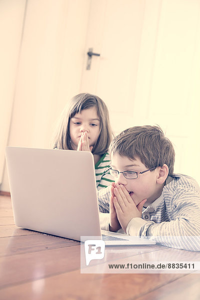 Brother and sister using laptop at home