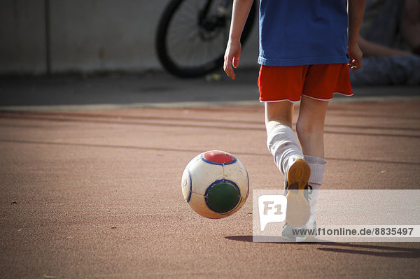 Boy kicking football on hard court  partial view