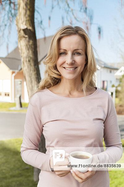 Lächelnde Frau mit Tasse Kaffee vor dem Wohnbereich