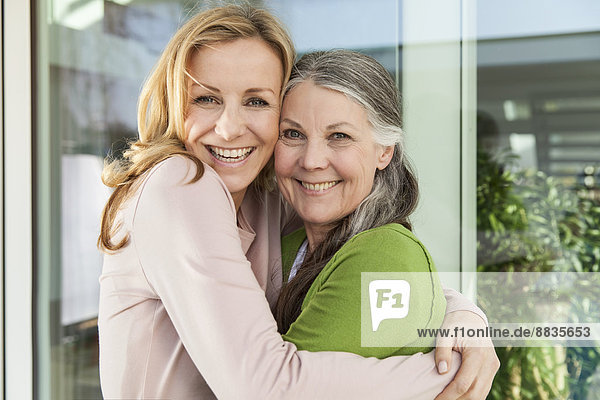 Seniorenmutter und ihre Tochter umarmen sich vor ihrem Haus.