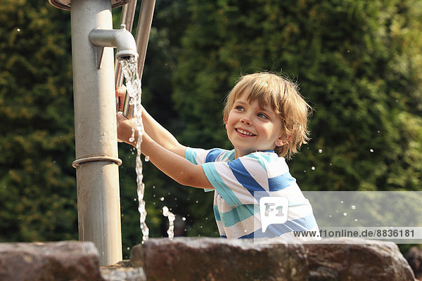 Porträt eines kleinen Jungen  der mit einer Wasserpumpe spielt.