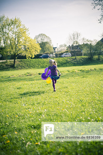 Little girl with balloons running on a meadow