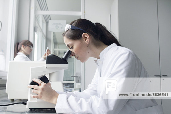 Portrait of young female student using microscope in lab