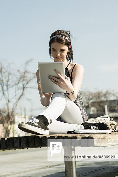 Junge Frau mit Tablet-Computer auf einer Bank sitzend