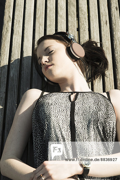 Junge Frau mit Kopfhörer auf einer Bank liegend